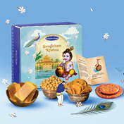Swagatham Krishna branded Krishna Jayanthi promotional graphic featuring a blue gift box, bowls of sweets, a peacock feather, and decorative text on a light blue background.